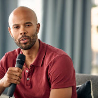 Cropped shot of a young man sitting on a sofa while speaking over a microphone